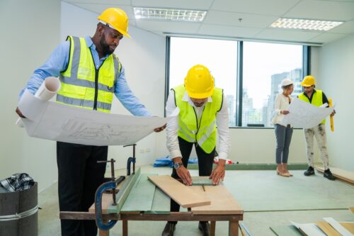 Architector and engineers with draft plan of building and laptop talking on constructing site. Construction manager and engineer working on building site in the office, teamwork.