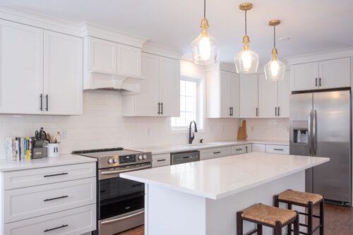 A modern white kitchen interior with an oven, sink, faucet, a wooden cabinet, and table